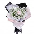 Pink rose surrounded by baby's breath in a bouquet with black and pink paper.