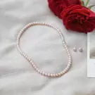 Pink pearl necklace and earrings on a white cloth with red roses.