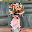 A large, colorful floral arrangement featuring gerbera daisies in pink, red, and yellow, presented on a stand.