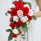 Cascading wedding bouquet of red and cream roses with red berries and eucalyptus leaves.