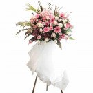 A tall, elegant floral arrangement with pink and white flowers on a stand, draped with white fabric.