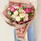 Bouquet of pink and white roses, daisies, carnations, and baby's breath in brown and pink wrapping.