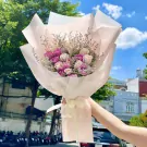 A hand holds a bouquet of pink and white roses, wrapped in delicate pink paper with a ribbon.