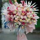 Floral arrangement in pink and orange tones with roses, daisies, and greenery.