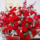 A bouquet of red roses, red orchids, and silver leaves in a red vase.