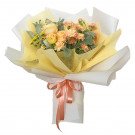 Peach and yellow roses and carnations in a bouquet with yellow and white paper wrap and pink ribbon.