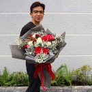 Man holding a bouquet of red and white roses with baby's breath, wrapped in grey paper and tied with a red ribbon.