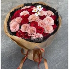 Bouquet of pink and red roses with white accent flowers, wrapped in brown paper and ribbons.