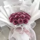 Amethyst pink bouquet of glittery roses, wrapped in white paper and netting, with decorative ribbons.