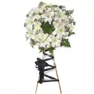 White funeral wreath with lilies, roses, and carnations on a wooden easel with black and white ribbons.