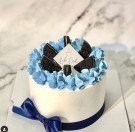 A white cake with blue frosting, Oreos, and a blue ribbon.