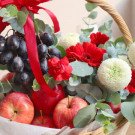 Fruit basket with grapes, apples, red gerbera daisies, white mums, and red carnations.