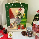 Christmas gift set with mugs, miniature tree, and festive decorations in a green box.