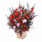 Red roses and pink carnations in a wooden basket with a brown ribbon.