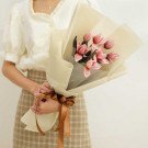 Bouquet of pink tulips wrapped in cream paper, tied with a brown ribbon.