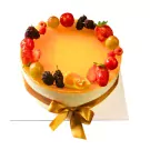 Round, orange mousse cake with fresh berries and fruits on top, tied with a golden bow.