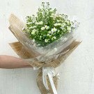 Bouquet of white aster flowers wrapped in brown paper and white tulle, tied with a white ribbon.