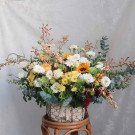 Flower basket with roses, gerberas, chrysanthemums, sunflowers, and various greens.