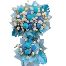 Two-tiered floral arrangement with blue and white flowers, green leaves, and blue paper wrap.