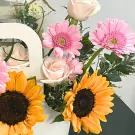 Bouquet of sunflowers, pink gerbera daisies, and light pink roses in a white basket.