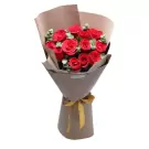 A bouquet of red roses with green leaves, wrapped in brown paper and tied with a gold ribbon.