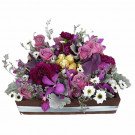 A wooden box filled with purple roses, carnations, orchids, and other flowers and leaves.