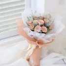 A bouquet of delicate pink cappuccino roses, wrapped in white and peach paper with a pale yellow ribbon.