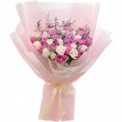 Bouquet of pink and lavender roses with delicate filler flowers, wrapped in pink paper and tied with a light yellow ribbon.