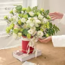 Bouquet of white lotuses, green carnations, and lisianthus in a red box.