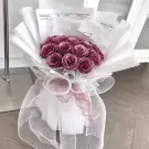 A bouquet of deep pink roses wrapped in white paper and tulle.