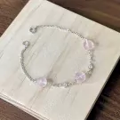 Silver bracelet with pink beads and small flower charms on a wooden surface.