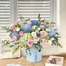 Bouquet of blue globe thistles, pink roses, and hydrangeas in a light blue box.