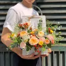 Person in white shirt holding a rectangular floral arrangement with roses and greenery.