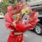 A red and pink bouquet filled with games like Monopoly, lotto, and playing cards, adorned with red berries.