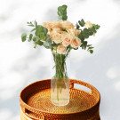 Bouquet of peach roses and eucalyptus in a glass vase on a woven tray.