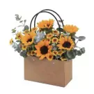 Brown paper bag filled with sunflowers and yellow daisies, accented with eucalyptus leaves.