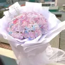 A bouquet of pink, blue, and white roses with a silver crown.