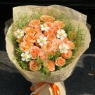 A bouquet of peach roses with small white flowers and green foliage, wrapped in light brown paper.