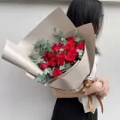 A bouquet of 24 red roses with eucalyptus, wrapped in beige paper and tied with a brown ribbon.