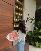 Woman holding a large bouquet of pink roses in front of a building with "Kay's" signage.
