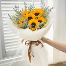 Sunflower bouquet with purple statice, wrapped in white paper and tied with a brown ribbon.
