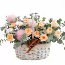 A white basket filled with peach roses, pink peonies, eucalyptus, and cotton balls.