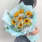 A bouquet of sunflowers and baby's breath wrapped in light blue paper.