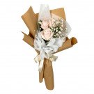 Bouquet of three pale pink roses with baby's breath, wrapped in brown paper and white sheer fabric.
