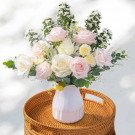 A bouquet of pink and white roses with yellow accents in a white vase.