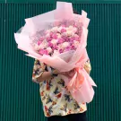 Pink and white roses in a large bouquet, wrapped in pink paper and tied with a bow.