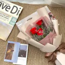 Bouquet of three red roses, wrapped in pale pink and cream paper, with a brown ribbon.