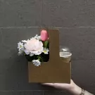 Brown cardboard caddy with pink tulip, peach peony, and daisies next to a covered cup.