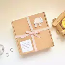 A gift box tied with pink ribbon, with a small card and wax seal, next to a candle.