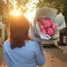 Woman holding bouquet of pink roses and carnations in the sunset.